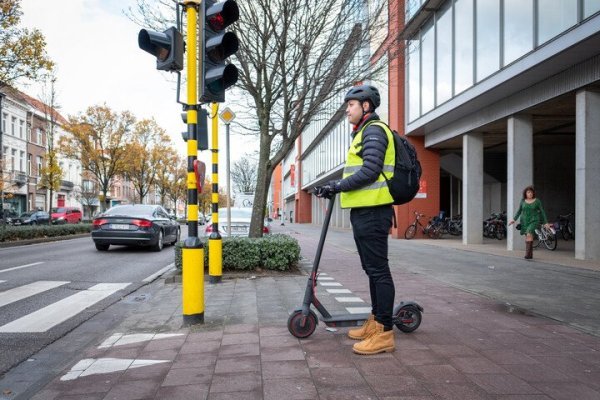 man naast e-step aan verkeerslichten